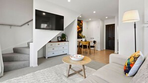 Een moderne woonkamer met een trap, een eethoek en een aan de muur bevestigde televisie.