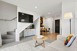 Un salon moderne avec un escalier, un coin repas et un téléviseur fixé au mur.