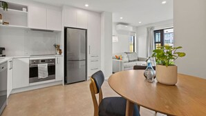 Een moderne keuken met witte kasten, een roestvrijstalen koelkast, en een eethoek met een houten tafel en stoelen.