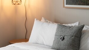 A neatly made bed with white linens, a gray pillow, and a white pillow. A framed picture hangs on the wall above the bed. - Trailside Charm | TART Trail | Downtown | (Traverse City)