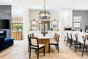 A modern kitchen with a large island, white cabinetry, and a dining area with chairs. - Twin Palms at PGA West, Heated Pool & Fire Pit (La Quinta)