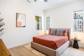 A bedroom with a bed, a bedside table, a window, and a wall-mounted artwork.
