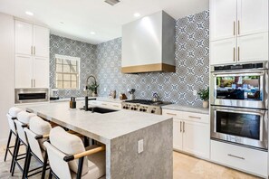 A modern kitchen with a central island, built-in oven, and patterned backsplash. - Twin Palms at PGA West, Heated Pool & Fire Pit (La Quinta)