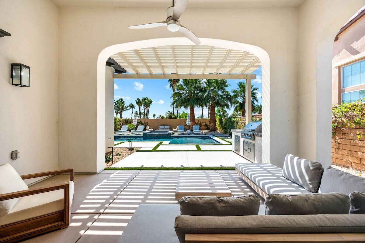 A modern outdoor living area with a pool, patio furniture, and a view of a backyard with palm trees.