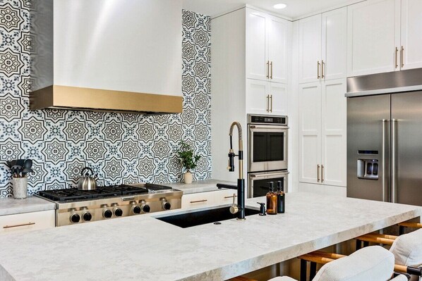 A modern kitchen with a central island, stainless steel appliances, and patterned backsplash.
