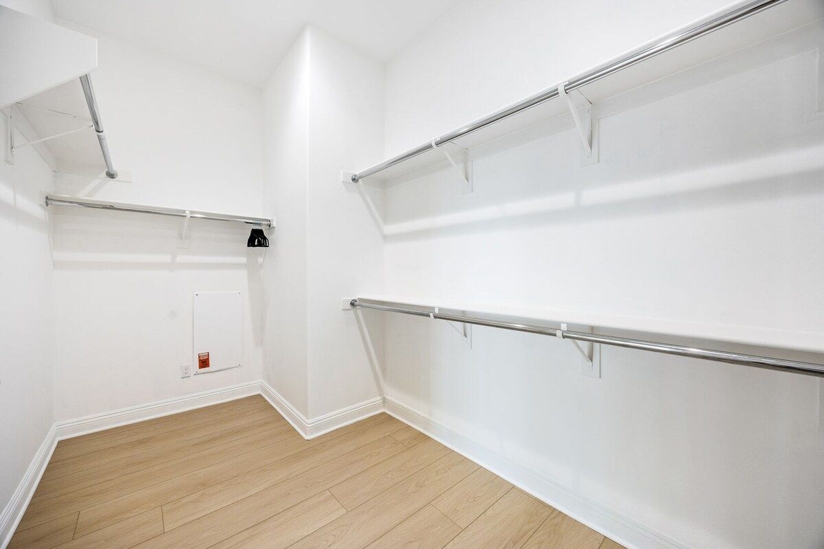 A room with white walls, a wooden floor, and a built-in closet with metal rods.