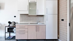 A compact kitchen with a microwave, kettle, and coffee maker on a small table, light wood cabinets, and a tiled backsplash. - Obelisk Studio - Lecce Selection (Lecce)