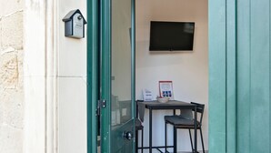 A narrow entrance with a green door, a small table with a chair, a flat-screen TV mounted on the wall, and a poster on the wall. - Obelisk Studio - Lecce Selection (Lecce)