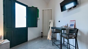 A small room with a dark green door, a white wall, a flat-screen TV mounted above a table with two chairs, and a poster on the wall. - Obelisk Studio - Lecce Selection (Lecce)
