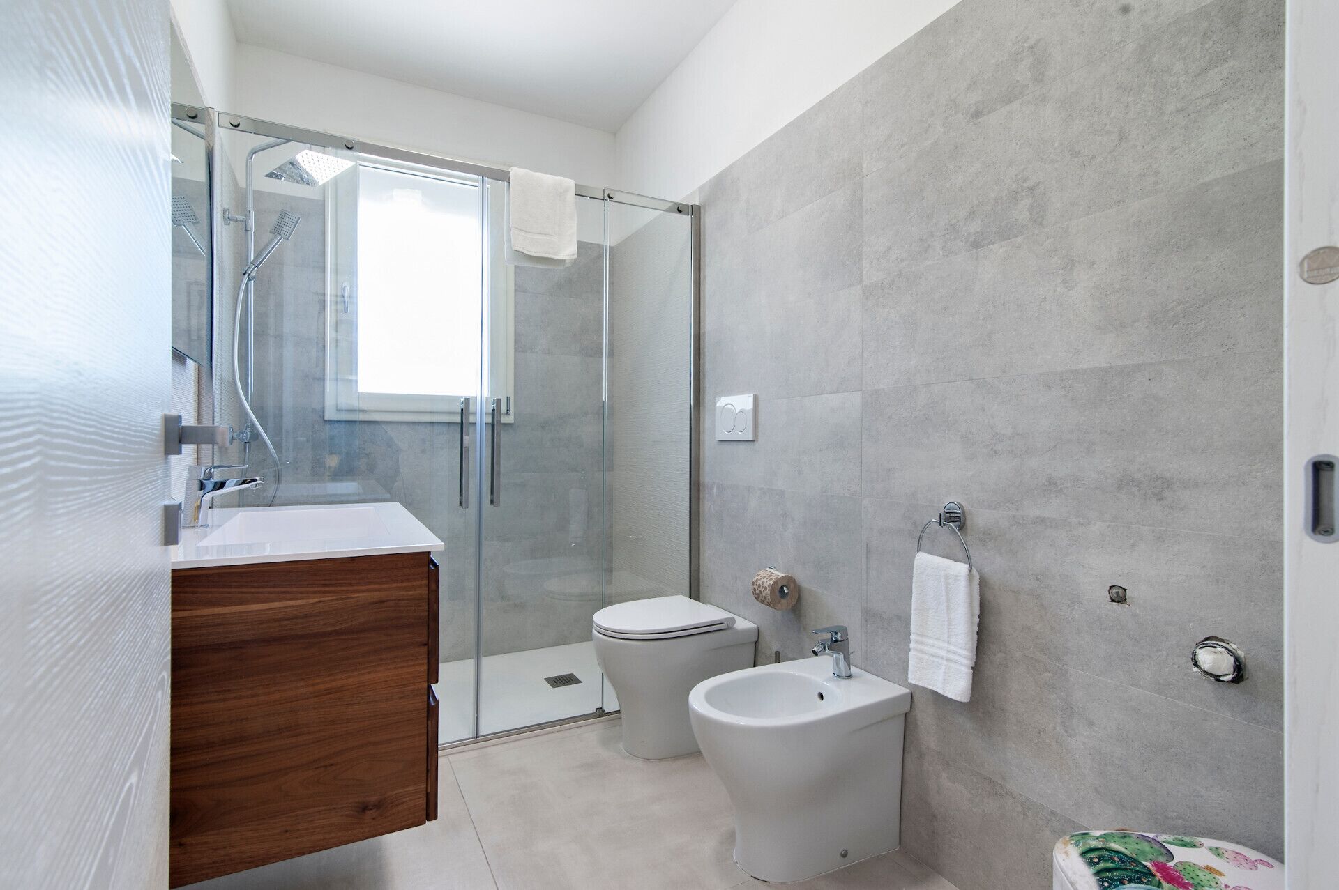 Une salle de bain moderne dotée d’une douche à parois de verre, de toilettes, d’un bidet et d’un meuble-lavabo en bois.