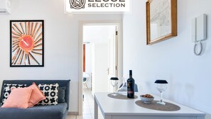 Un salon moderne avec un canapé, une table basse sur laquelle se trouvent des verres à vin et une bouteille, et une œuvre d’art encadrée accrochée au mur.