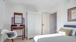 A bedroom with a bed, a chair, a dresser, a wardrobe, and a bedside table with a lamp.