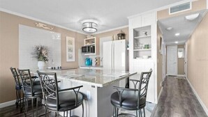 Una cocina moderna con una isla central, taburetes de bar, armarios blancos y un microondas.