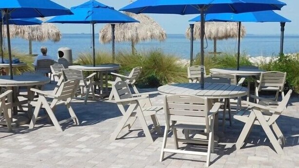 Terraza al aire libre con sombrillas azules y de paja, dispuesta en un patio empedrado con vistas al mar.