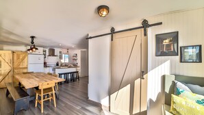 A spacious kitchen with a wooden table and bench, a sliding barn door, and a dining area with a bench and a sofa.