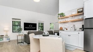 A modern kitchen with white cabinetry, a stainless steel refrigerator, and a dining area with a round table and chairs. - Oak Valley | King Bed, Sun Deck & Outdoor Shower, Full Kitchen, Fire-pit (Fredericksburg)