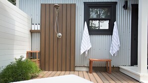 A small outdoor shower area with a wooden door, a bench, and two towels hanging on the wall. - Oak Valley | King Bed, Sun Deck & Outdoor Shower, Full Kitchen, Fire-pit (Fredericksburg)