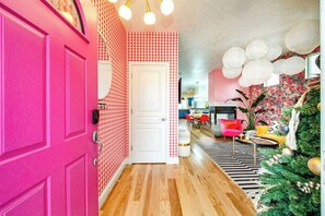 A hallway with a pink door, patterned wallpaper, a wooden floor, and a Christmas tree with decorations.