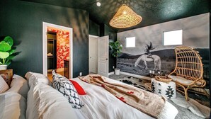 A bedroom with a bed, a rattan chair, a wall mural, and a door leading to another room. - The Audacity Boise - BSU -Close to eveything ! (Boise)