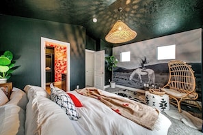 A bedroom with a bed, a rattan chair, a wall mural, and a door leading to another room.