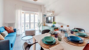 A modern living room with a sofa, dining table set for six, and a large window. - Como Hills - MyHomeinComo (Como)