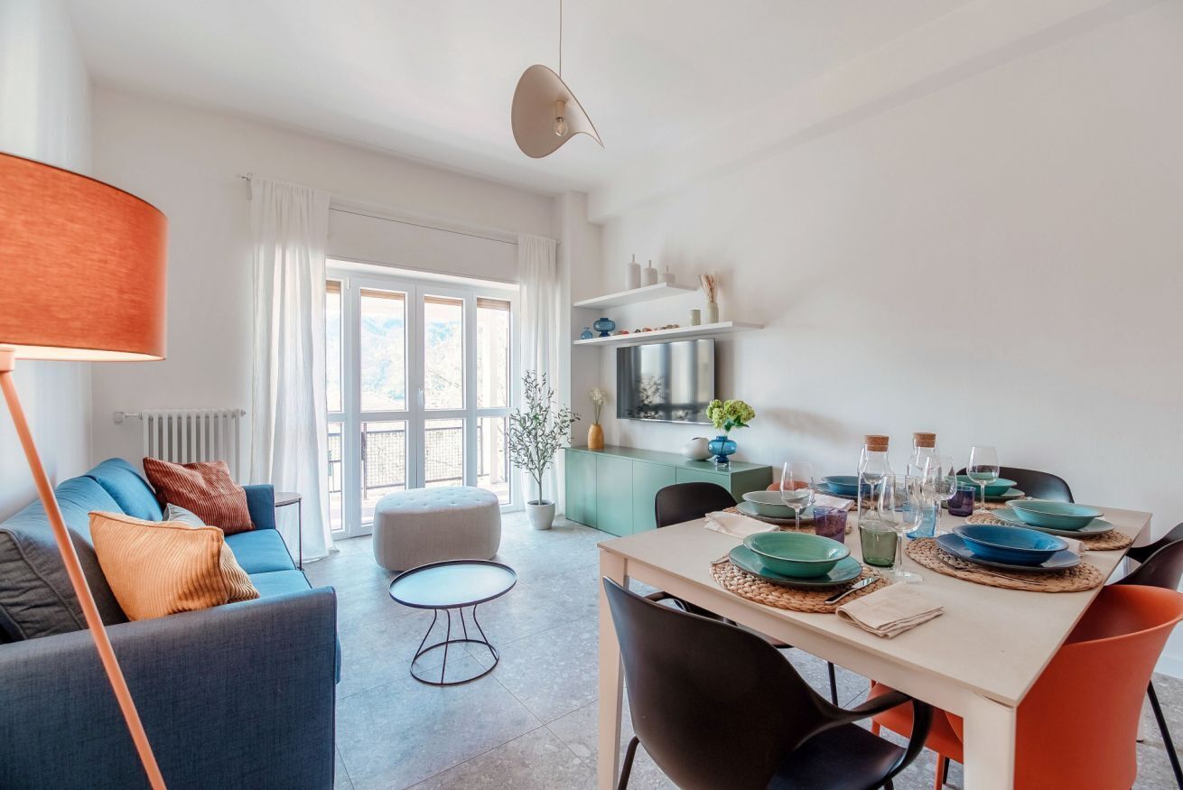 A modern living room with a sofa, a dining table set with plates, and a kitchen area with a refrigerator.