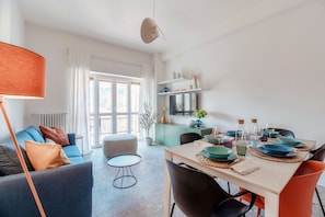 A modern living room with a sofa, a dining table set with plates, and a kitchen area with a refrigerator.