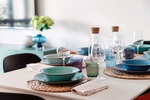 A dining table set with blue plates, clear glasses, and a woven placemat.