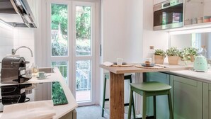 A modern kitchen with a coffee machine, a wooden table, and green stools. - Como Hills - MyHomeinComo (Como)