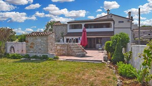 A two-story house with a stone exterior, a tiled roof, and a small garden area with a red umbrella.
