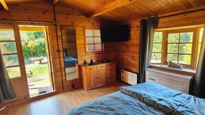 A wooden cabin bedroom with a bed, dresser, and a TV mounted on the wall. - Vacation home "Im Wäldchen" near the lake for couples and families with pets (Templin)