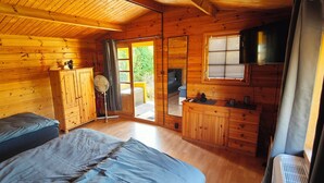A wooden cabin with two beds, a small kitchenette, and a large window. - Vacation home "Im Wäldchen" near the lake for couples and families with pets (Templin)