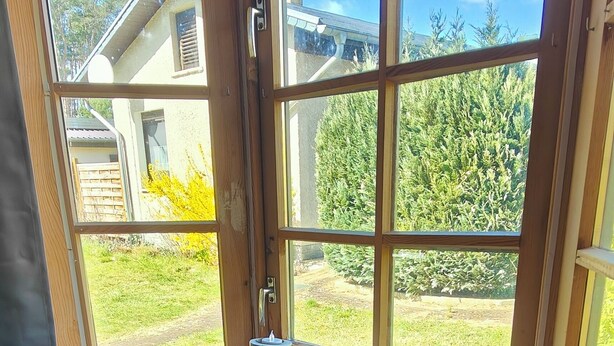 A room with a large window, a built-in air conditioner, and a small shelf with decorative items. - Vacation home "Im Wäldchen" near the lake for couples and families with pets (Templin)
