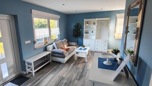 A modern living room with a sofa, coffee table, and a white console table. There is a large mirror and a window with a view of greenery. - Vacation home "Im Wäldchen" near the lake for couples and families with pets (Templin)