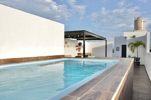 A rooftop swimming pool with a wooden deck, a covered seating area, and a water tank. - Rincon Colonial Apartments (Mazatlán)