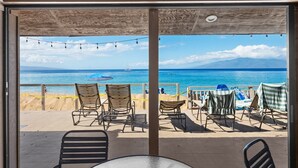 Uitzicht op het strand vanaf een balkon met stoelen en een tafel, met zicht op de zee en een berg in de verte.