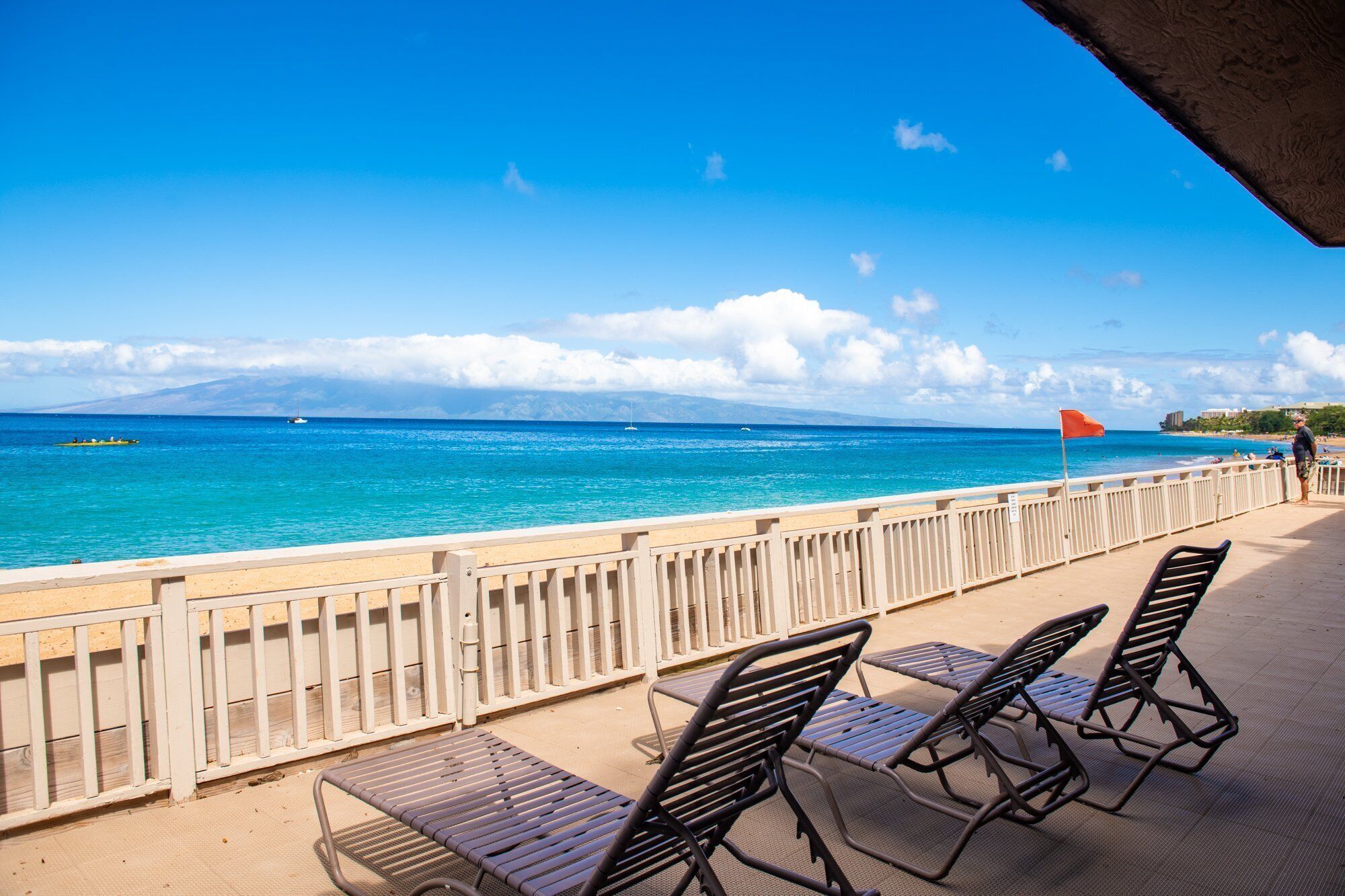 A beachside view with a railing, a flag, and lounge chairs.
