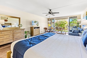 Ein geräumiges Schlafzimmer mit einem großen Bett, einer Holzkommode, einem Fernseher und einem Balkon mit Sitzgelegenheit.