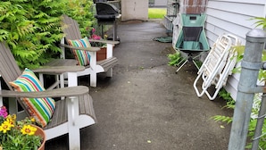 Een smal buitenterreinpad met twee Adirondack stoelen, een barbecue en een kruiwagen.