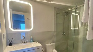 Une salle de bain moderne avec une douche à parois de verre, un lavabo blanc avec un miroir et des toilettes.