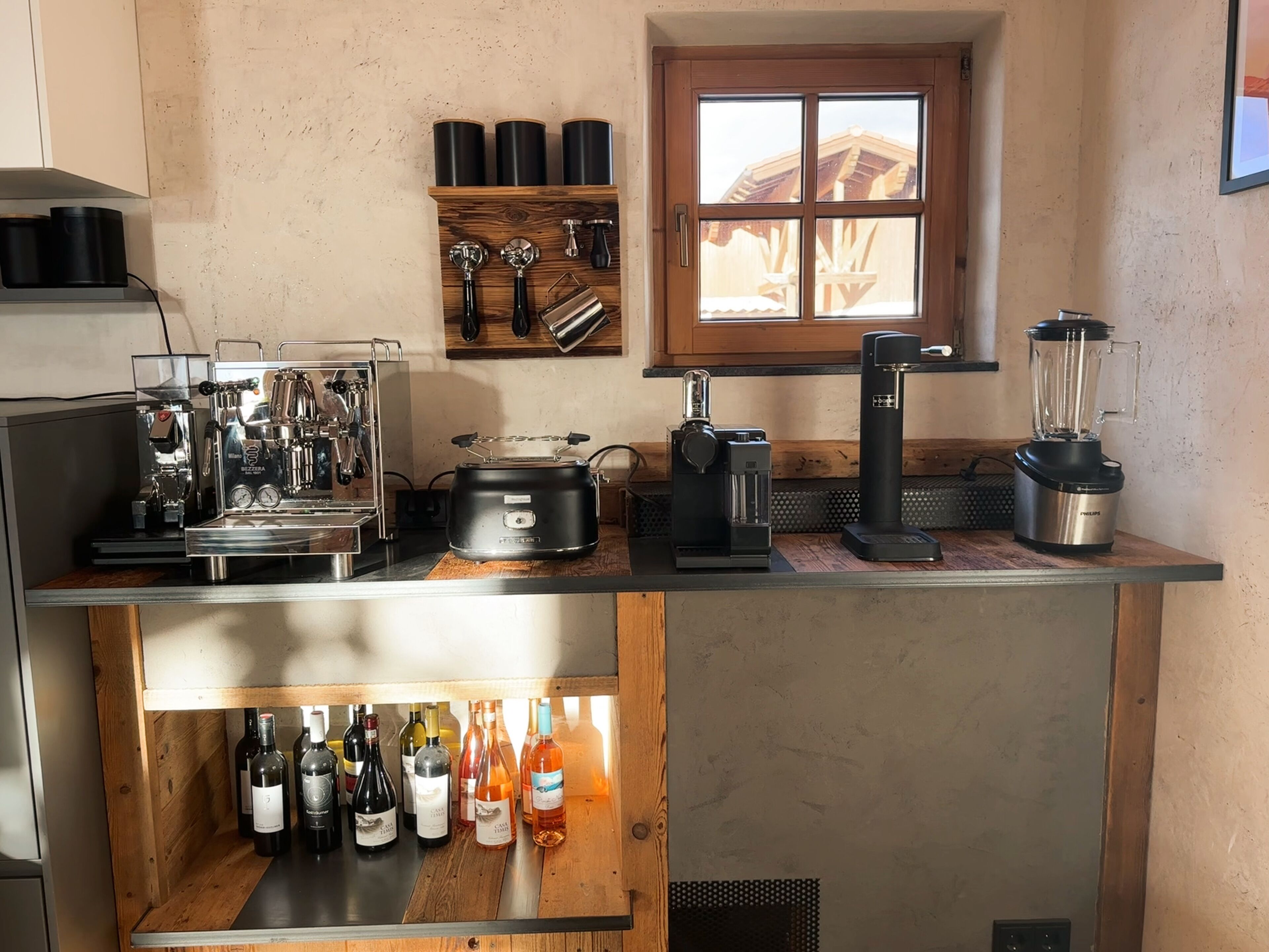 Una cocina con cafetera, licuadora y una estantería para vinos con botellas.
