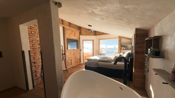 A bedroom with a large bathtub, a wooden wall, and a view of the sea.