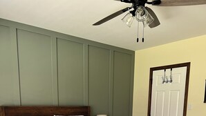 A neatly made bed with a striped bedspread, a wooden headboard, a nightstand with a lamp, and a door with a handle. - The Cozy Cottage! Private 1-bedroom cottage in a peaceful setting in Ottsville (ottsville)