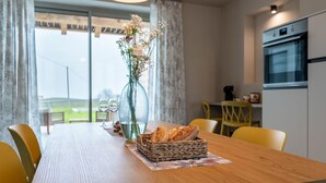 Un coin repas avec une table en bois, des chaises jaunes, un panier à pain en osier et un vase rempli de fleurs.
