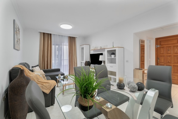A modern living room with a sofa, a coffee table, a potted plant, and a TV.