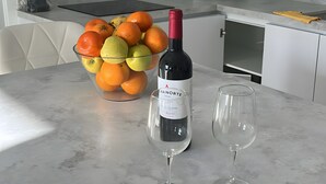 Una cucina con un piano di lavoro in marmo, una ciotola di frutta, una bottiglia di vino e due bicchieri da vino.