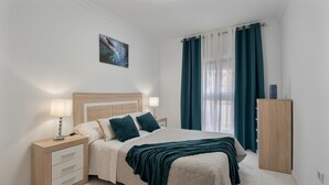 Una camera da letto con un letto, comodini, un armadio, una finestra con tende e un quadro appeso al muro.