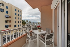 A balcony with a table and chairs, a potted plant, and a view of the street and buildings.