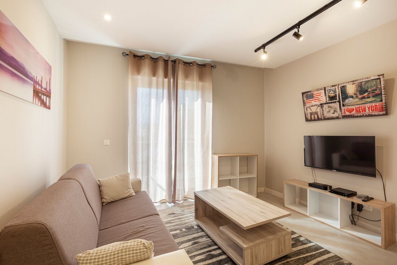A modern living room with a sofa, coffee table, TV, and artwork on the wall.
