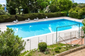 A rectangular swimming pool with a white fence, surrounded by greenery and white lounge chairs.